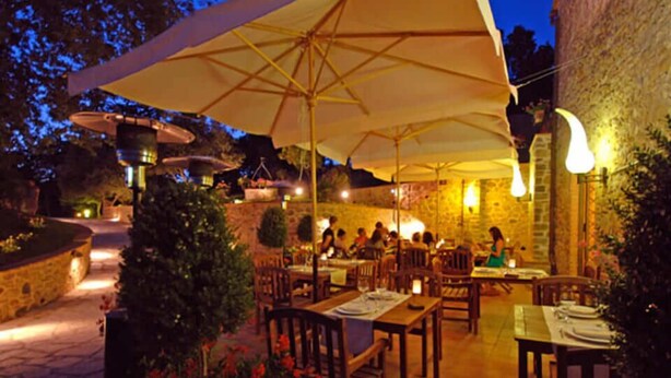 Un espace extérieur aménagé pour les repas, avec des tables et des chaises, de grands parasols et des murs en pierre.