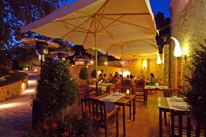 An outdoor dining area with tables and chairs, large umbrellas, and stone walls. - Locanda all'Andreas (Manciano)