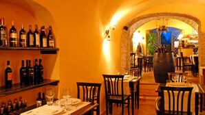 Un restaurant à l’ambiance chaleureuse, avec une arche en briques qui mène à la salle à manger. On y trouve de nombreuses tables et chaises, ainsi qu’une variété de bouteilles de vin exposées sur des étagères.