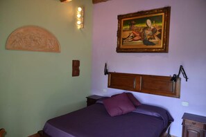 A bedroom with a bed, a headboard, a wall-mounted painting, and a wall-mounted light fixture. - Locanda all'Andreas (Manciano)