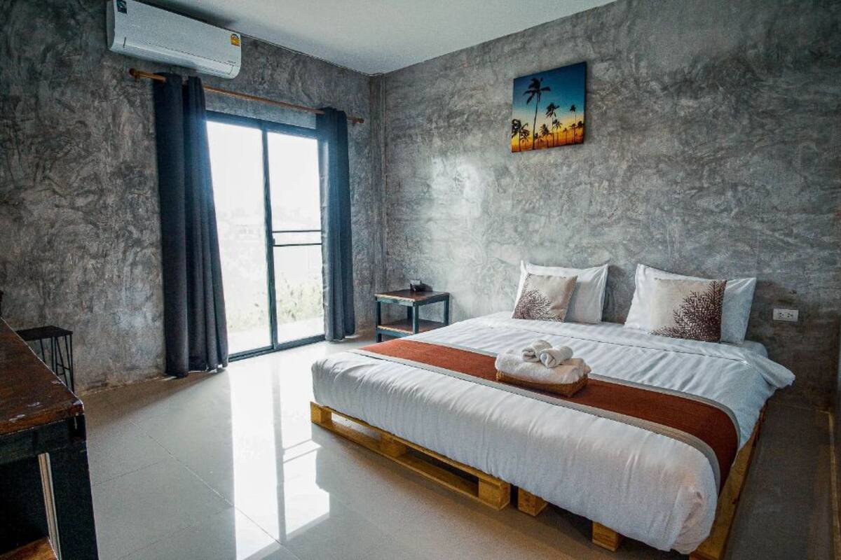 A bedroom with a large bed, a small side table, a nightstand, and a window with curtains.