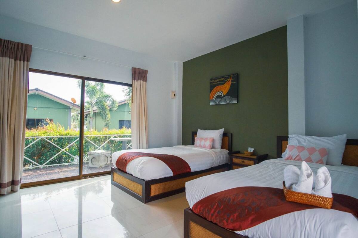 A hotel room with two beds, a balcony with a view, and a painting on the wall.