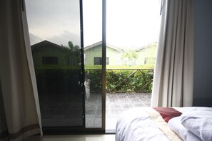 Une chambre avec un lit, une porte-fenêtre coulissante donnant sur un balcon avec vue sur un immeuble et de la verdure.