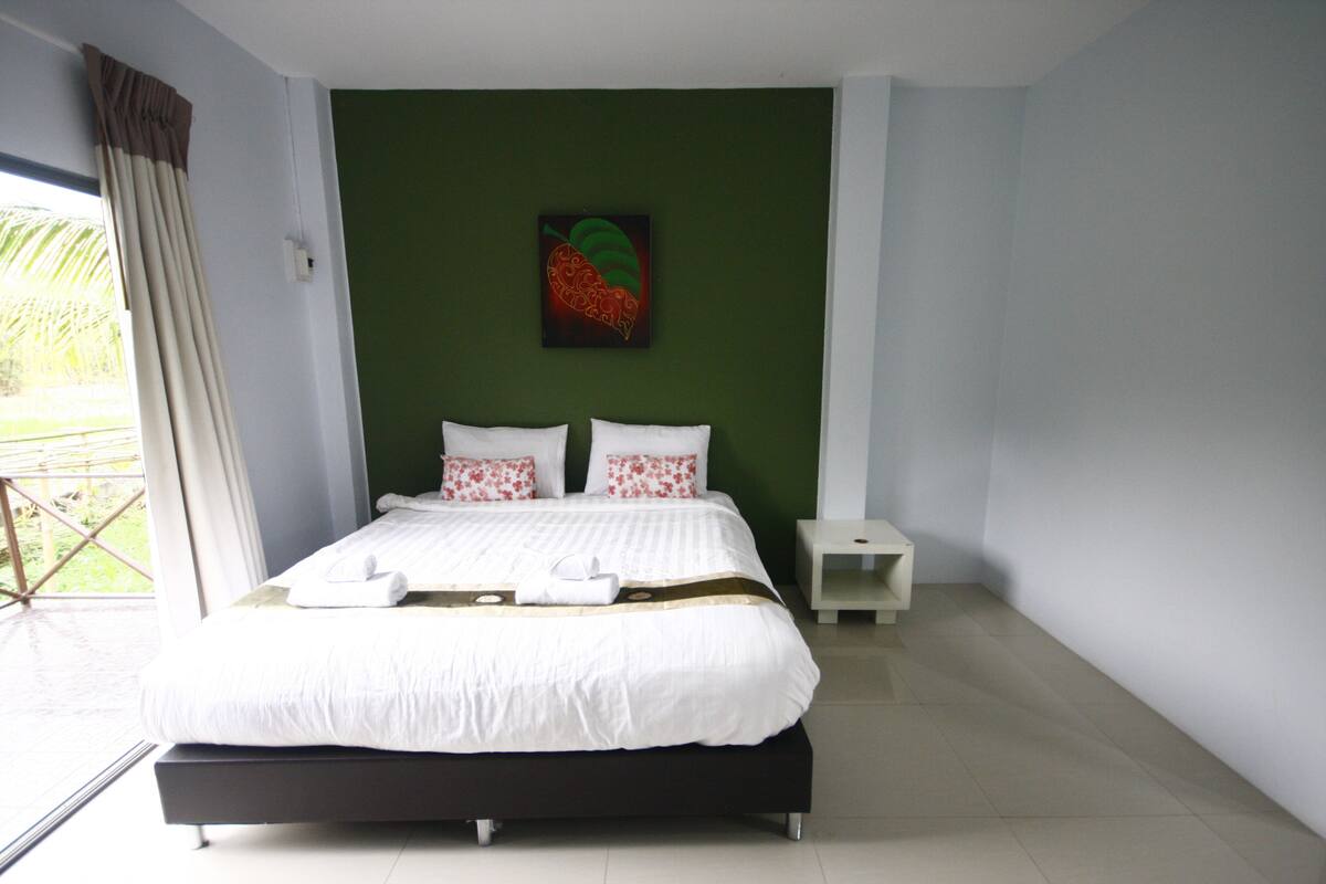 A modern bedroom with a large bed, green walls, and a tropical view.