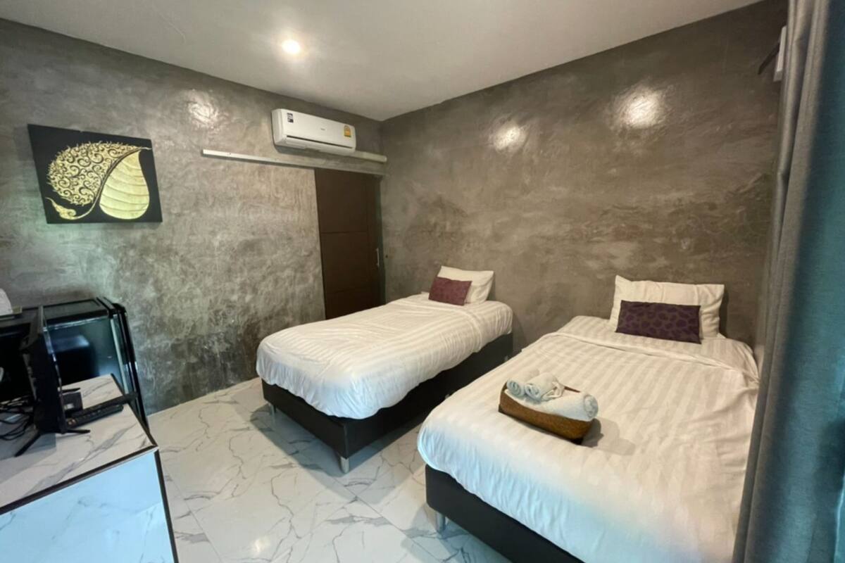 A hotel room with two beds, a marble floor, an air conditioning unit, and a small desk with a computer.