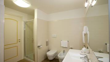 A bathroom with a shower, toilet, bidet, and sink.