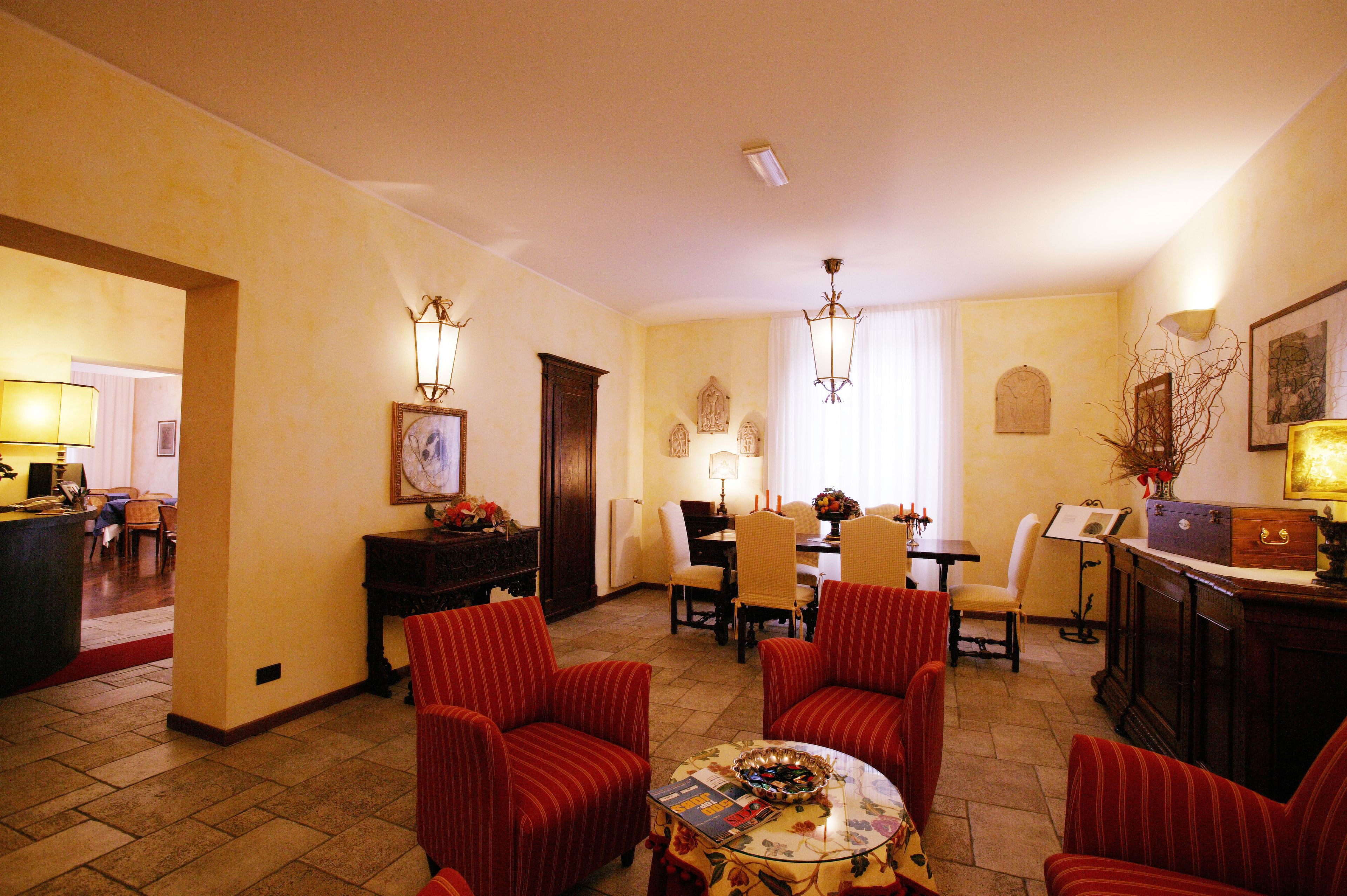 A hotel lobby with red upholstered chairs, a dining area with a piano, and a reception desk.