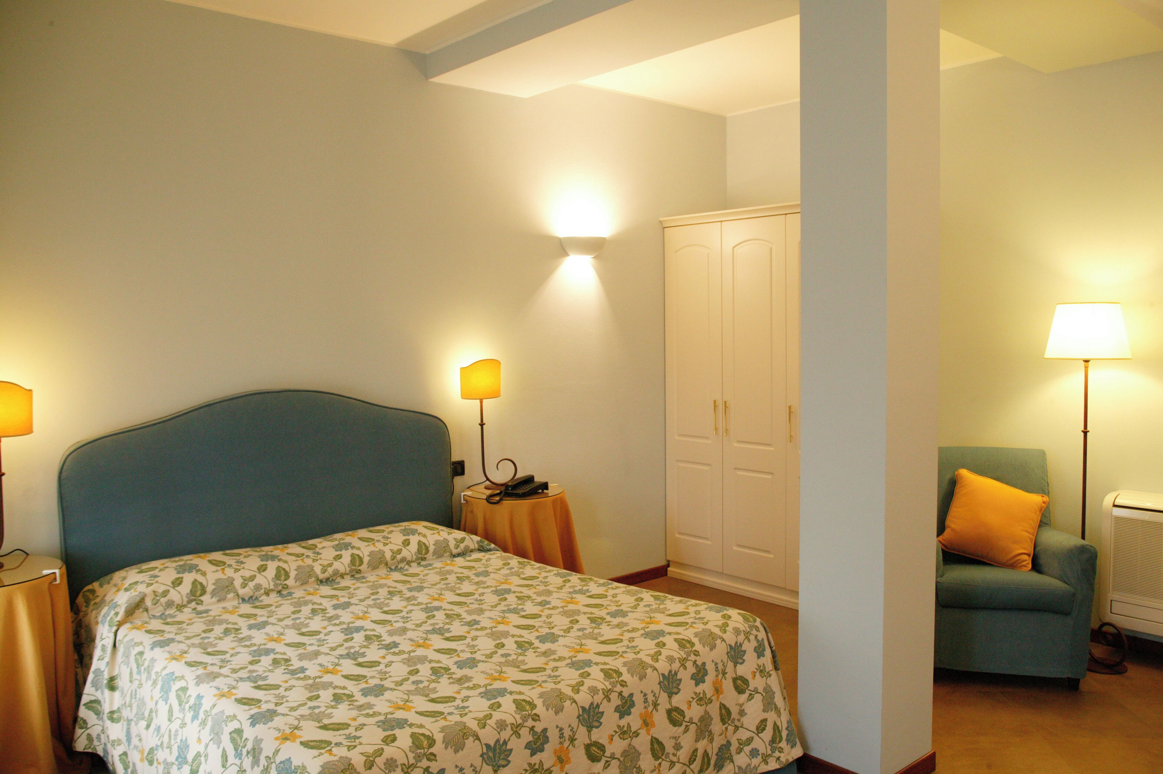 A bedroom with a bed, bedside lamps, a wardrobe, and a chair.