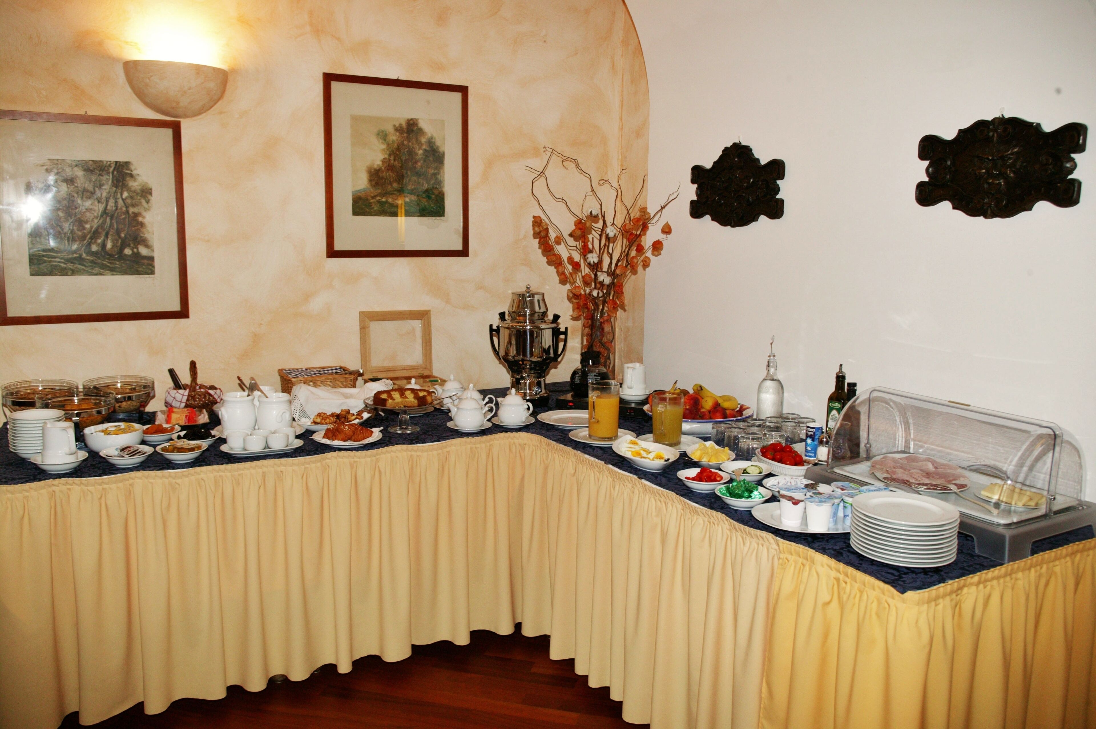 Una mesa de buffet con diferentes alimentos y bebidas, marcos con fotografías en la pared y un adorno decorativo.
