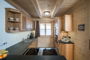 A compact kitchen with wooden cabinets, a built-in stove, and a window with curtains. - Apartment 2 - Ground floor - Apartment Tegernsee, Family Schneider, Kreuth (Kreuth)