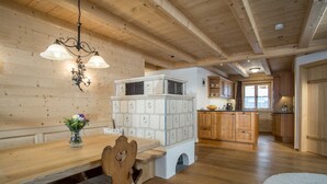 A wooden interior with a dining table, chairs, a chandelier, and a kitchen area.