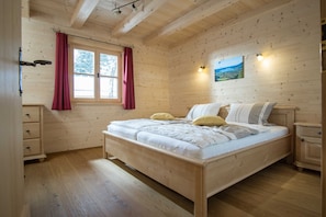 A wooden-paneled bedroom with a bed, a nightstand, a dresser, and a window with curtains. - Apartment 2 - Ground floor - Apartment Tegernsee, Family Schneider, Kreuth (Kreuth)