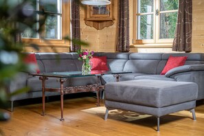 Ein modernes Wohnzimmer mit einem grauen Ecksofa, einem Glastisch und Holzböden.