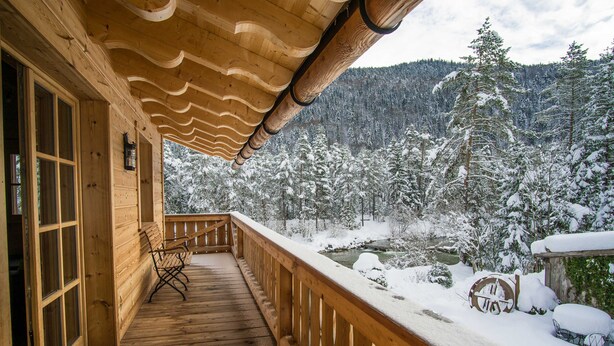 A wooden deck with a railing, a bench, and a view of a snowy forest.
