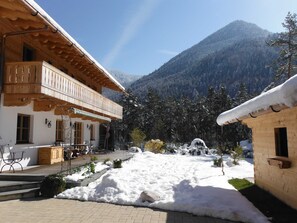 Ein traditionelles Holzchalet mit Balkon, gepflastertem Innenhof und Bergelandschaft im Hintergrund.