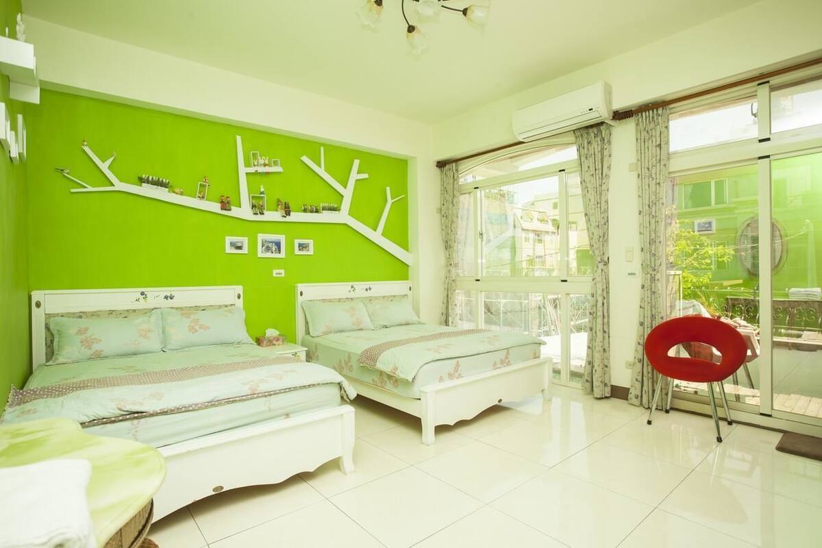 Un dormitorio con dos camas, una pared verde y un balcón con cortinas.
