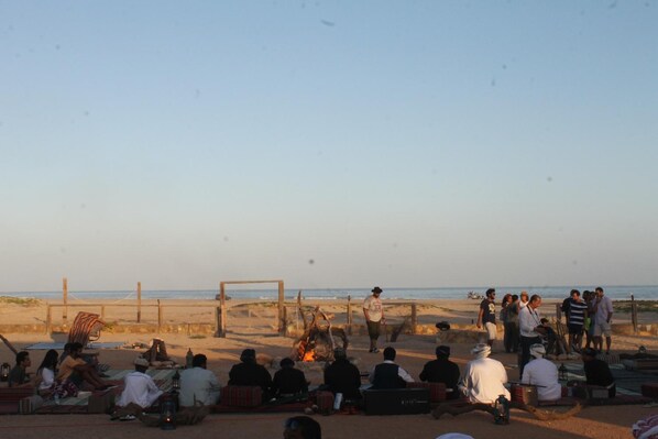 A beach scene with people gathered around a fire, some sitting and others standing. - Souly Eco Lodge (Taqah)