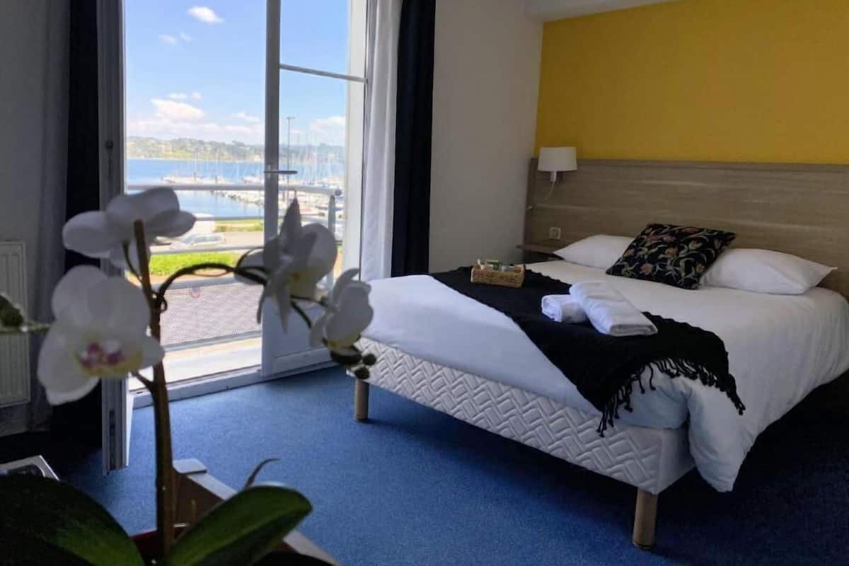 Ein Hotelzimmer mit Bett, Blick auf ein Gewässer und Fenster mit Stadtansicht.