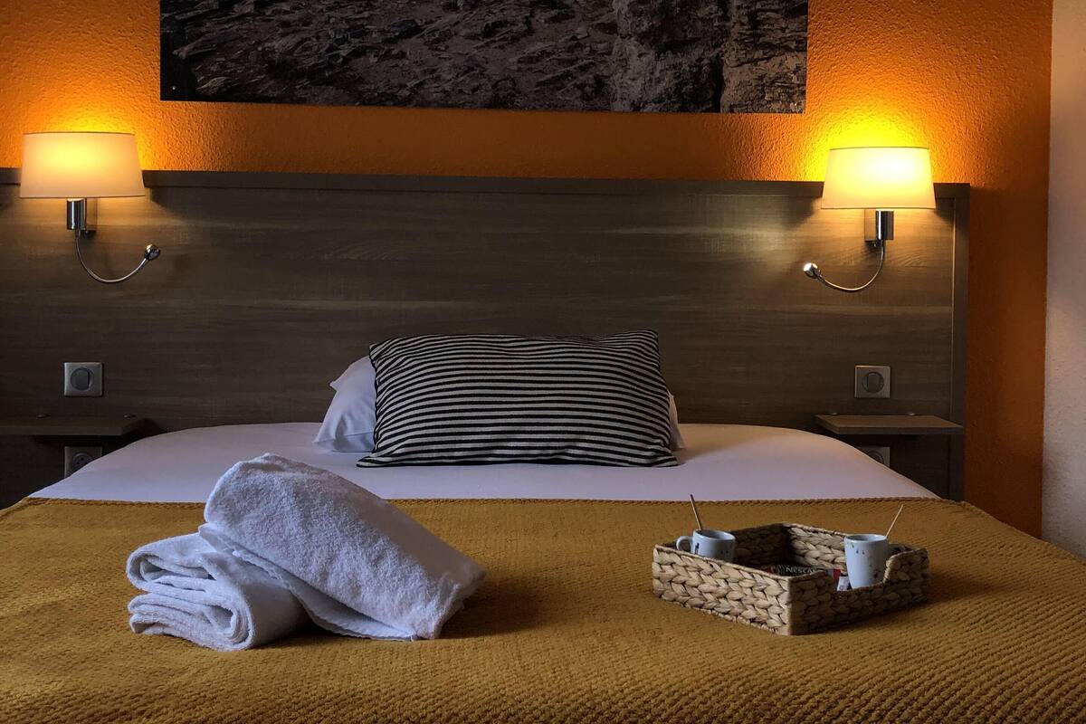 Ein Hotelzimmer mit einem Bett, zwei Nachttischlampen, einem Gemälde einer Küstenlandschaft und einem Tisch mit Tablett.