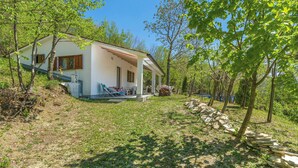 Ein eingeschossiges Haus mit Terrasse, umgeben von Bäumen und einer Steinmauer.