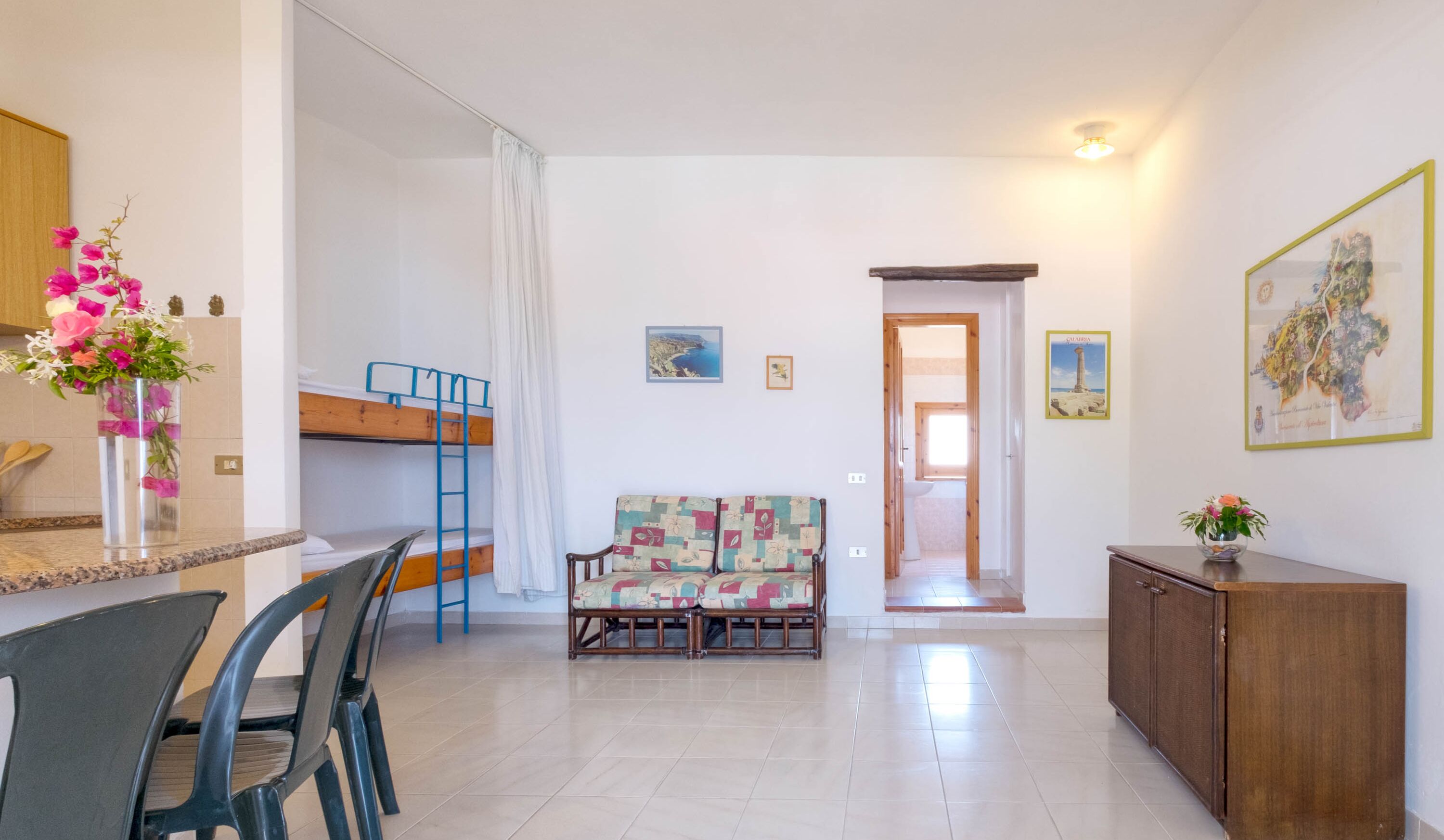 A room with a bunk bed, a sofa, a dining table with chairs, and a cabinet.
