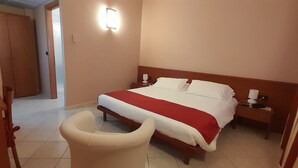 Una habitación de hotel con cama, mesitas de noche, una silla y una planta en maceta.