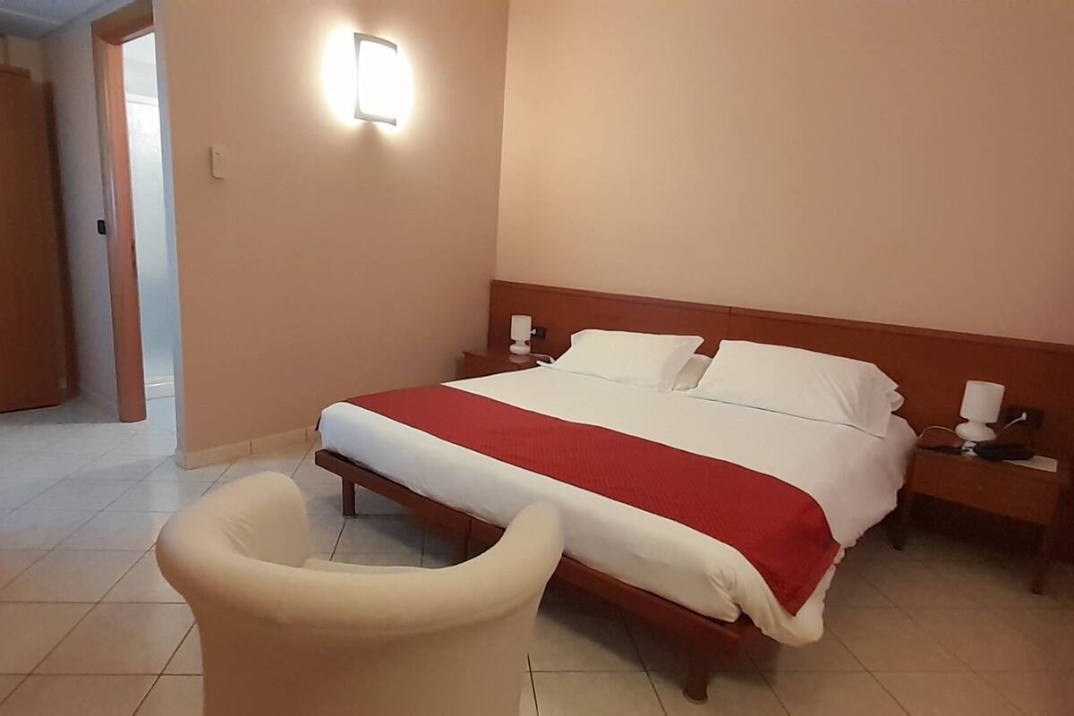 A hotel room with a bed, bedside tables, a chair, and a potted plant.