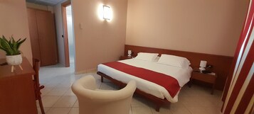 Quarto de hotel com cama, mesas de cabeceira, uma cadeira e um vaso de planta.