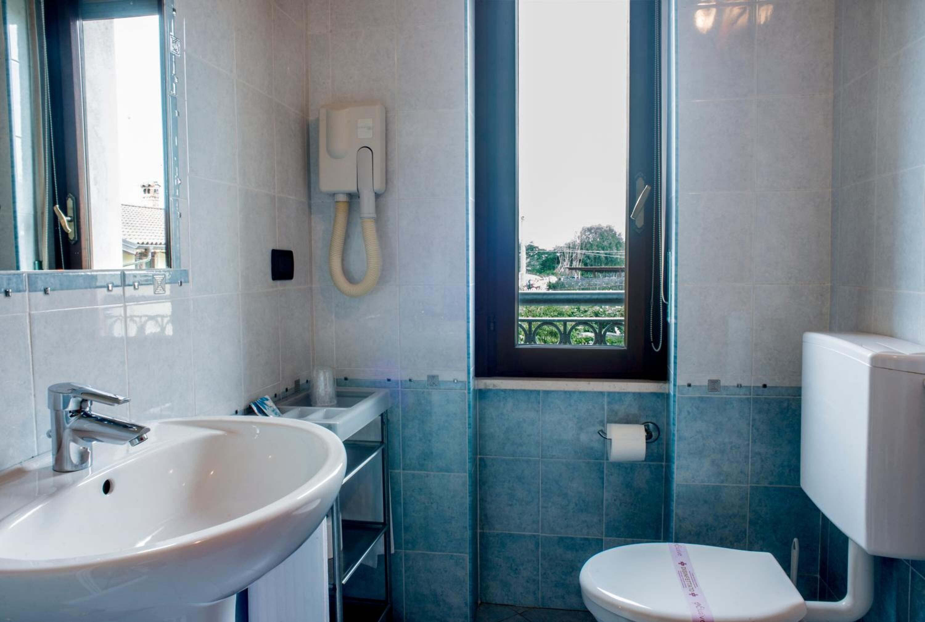 Un baño con lavamanos, inodoro y ventana con vista a la vegetación.