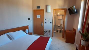 A hotel room with a bed, a bedside table, a TV mounted on the wall, and a bathroom visible through an open door.