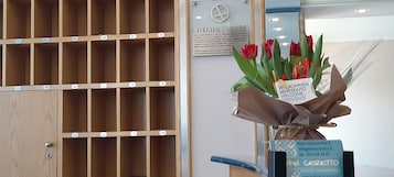 Área de recepção de hotel com painel de parede de madeira, placa de boas-vindas e informações de contato do hotel.
