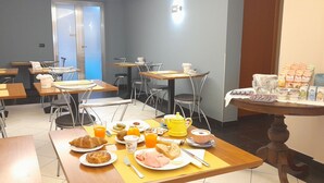 Comedor con mesas, sillas y alimentos para el desayuno, incluyendo cruasanes, jugo de naranja y yogur.