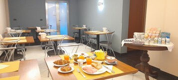 Uma área de refeições com mesas, cadeiras e itens de café da manhã, como croissants, suco de laranja e iogurte.