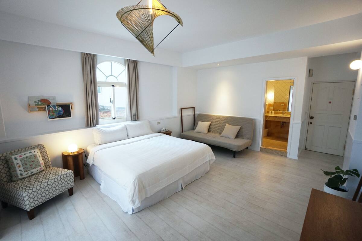 A modern bedroom with a large bed, a sofa, a chair, and a small table.