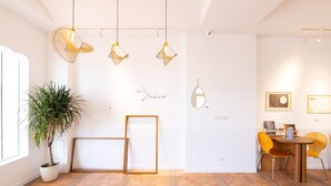 A modern interior with a potted plant, hanging light fixtures, a dining area with yellow chairs, and a wall with a mirror and framed artwork. - OwlStay The Salt (Hualien City)
