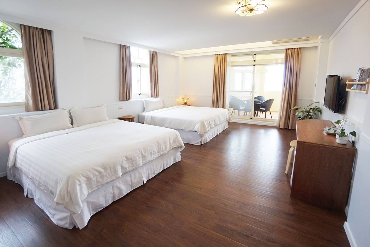 A hotel room with two beds, a desk, a chair, and a TV.