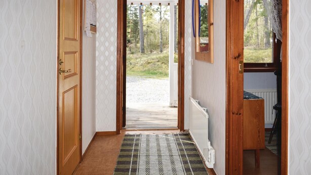 Un couloir avec une porte en bois, un tapis à motifs et une vue sur une forêt.