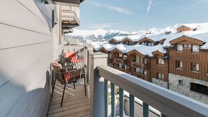 A wooden deck with outdoor furniture, overlooking snow-covered mountains and chalet-style buildings. - Le K2 Djola (Courchevel)