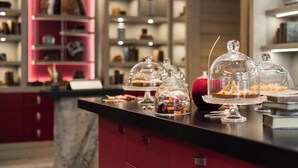 A dessert display with various covered items on a counter, a pink sign with the word "DJOOLA," and shelves with various items in the background. - Le K2 Djola (Courchevel)