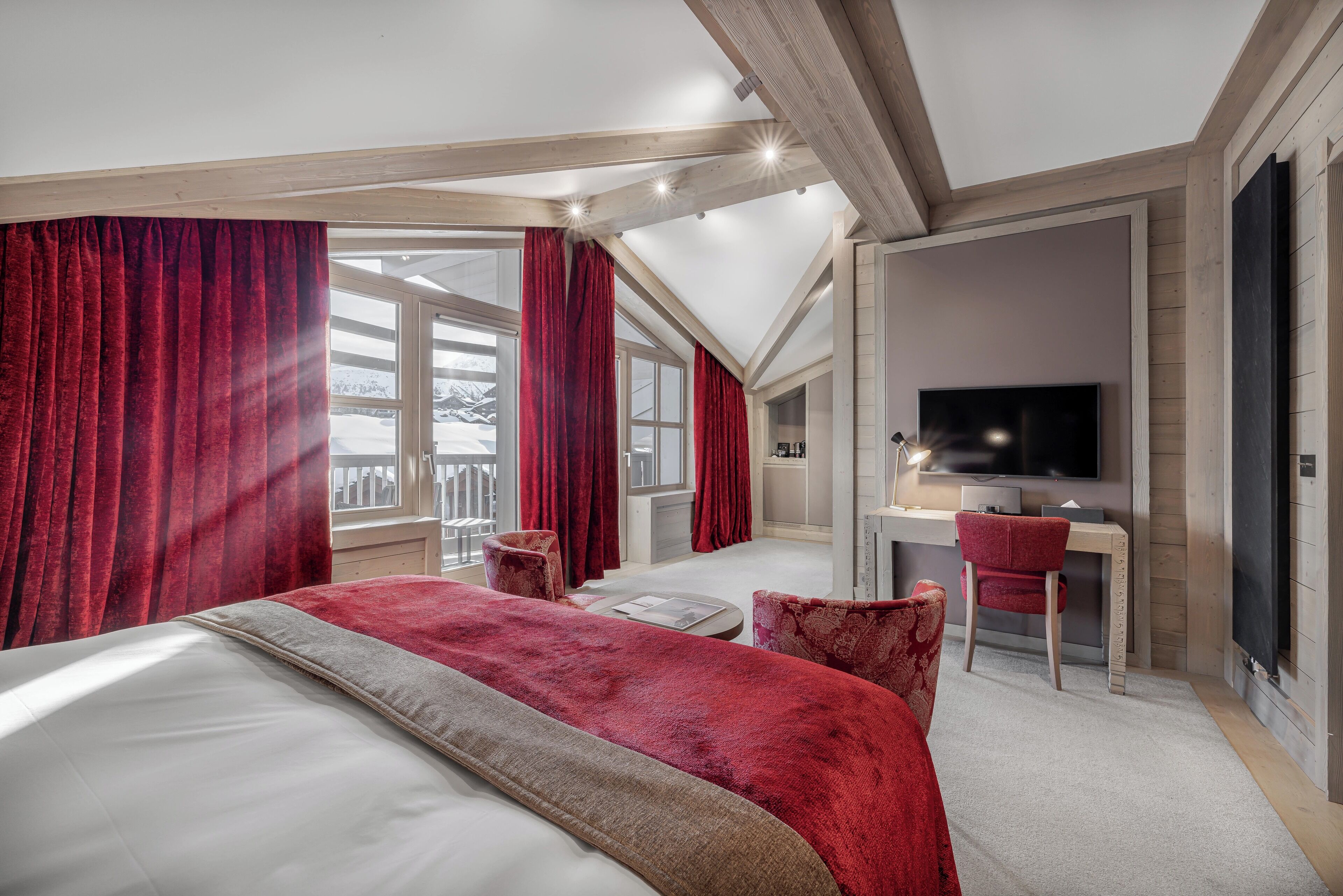 A modern bedroom with a large bed, red curtains, a desk, and a TV.