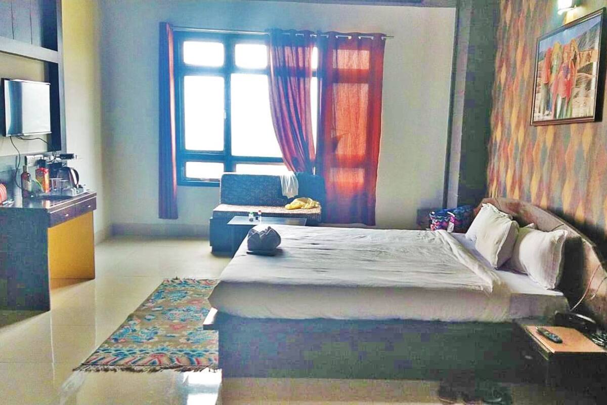 Habitación de hotel con una cama, un escritorio con computadora, una silla, una ventana con cortinas y un cuadro en la pared.