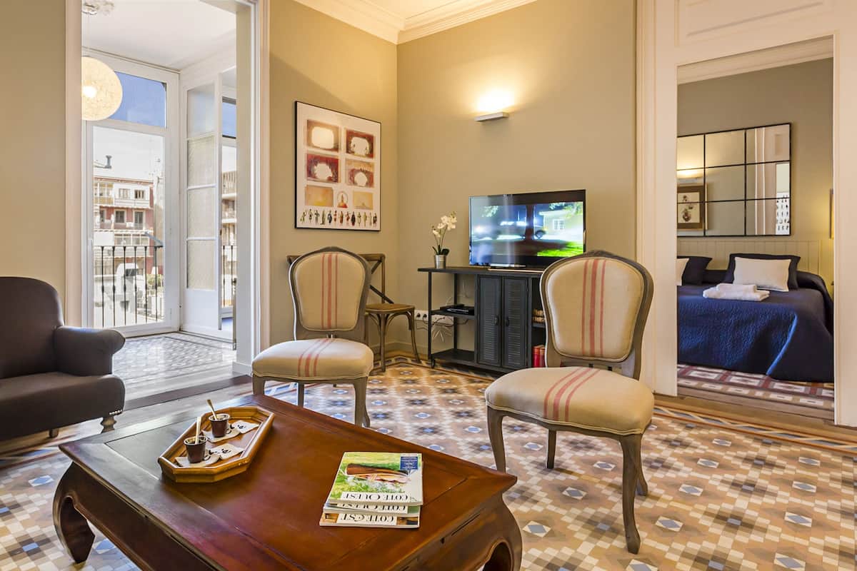 Une chambre d’hôtel avec une grande fenêtre, une télévision, une table à manger avec un plateau de nourriture et un lit recouvert d’une couverture bleue.