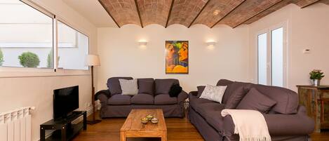 Una sala de estar con dos sofás, una mesa de centro de madera, un televisor sobre un mueble bajo y un cuadro en la pared.