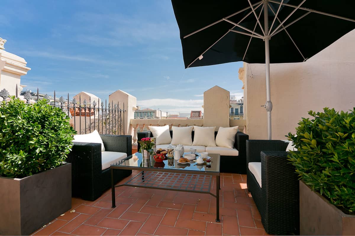 Une terrasse sur le toit, aménagée avec du mobilier d’extérieur, une table en verre et un grand parasol.