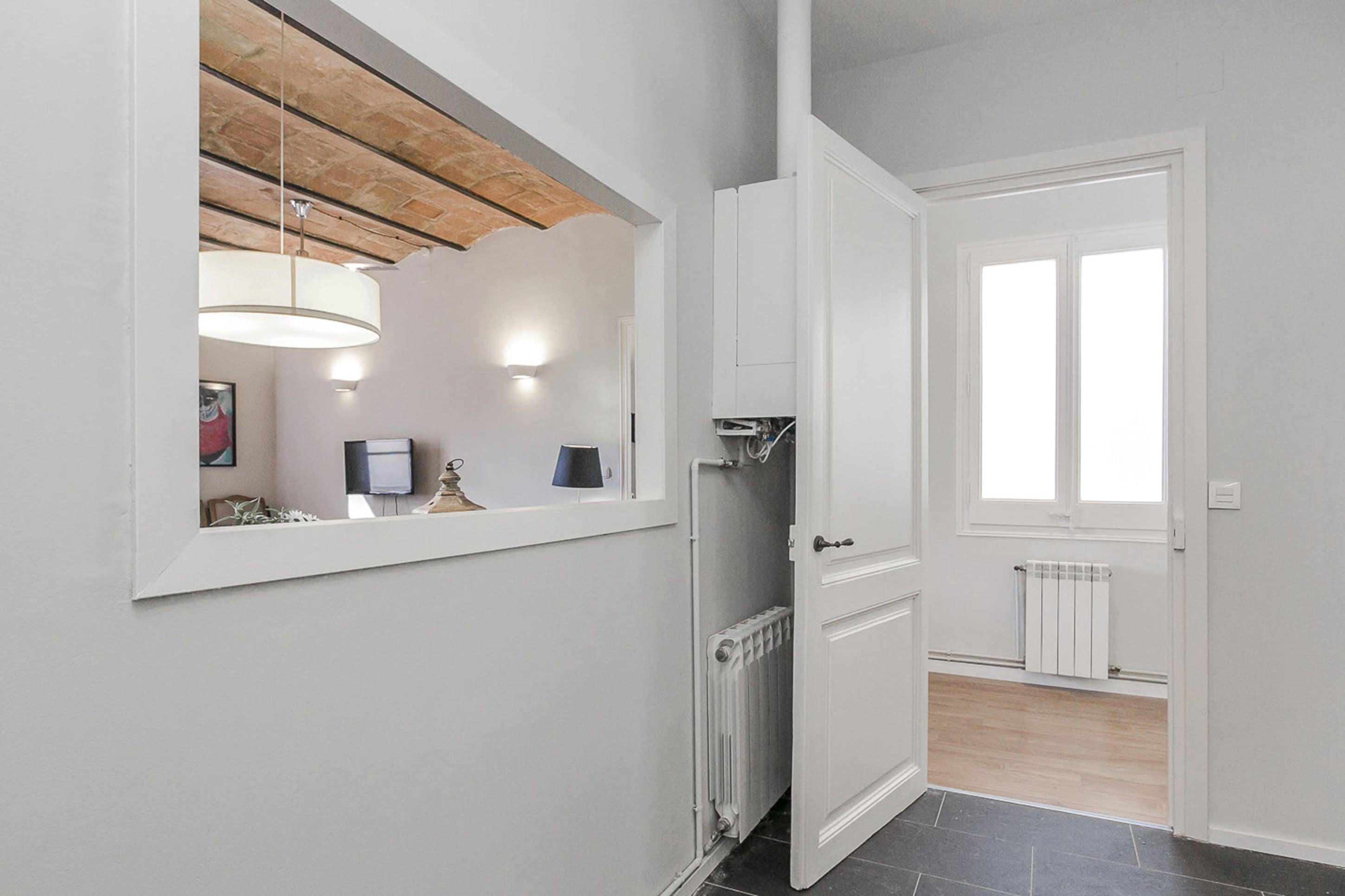 A hallway with a wooden ceiling, a white door, a radiator, and a window.