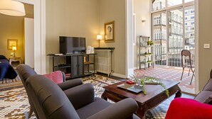 A modern living room with a sofa, a coffee table, a TV, and a large window with a view of buildings. - BCN Paseo de Gracia Rocamora Apartments (Barcelona)