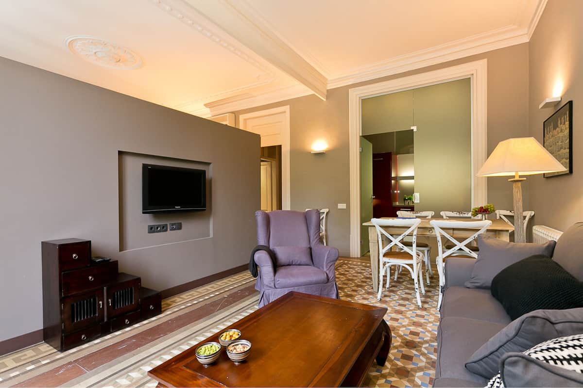 Un salon avec un téléviseur à écran plat, un fauteuil violet, une table basse en bois et un canapé.