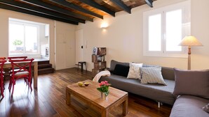 A spacious living area with a wooden coffee table, a sofa with cushions, and a dining area with red chairs. - BCN Paseo de Gracia Rocamora Apartments (Barcelona)