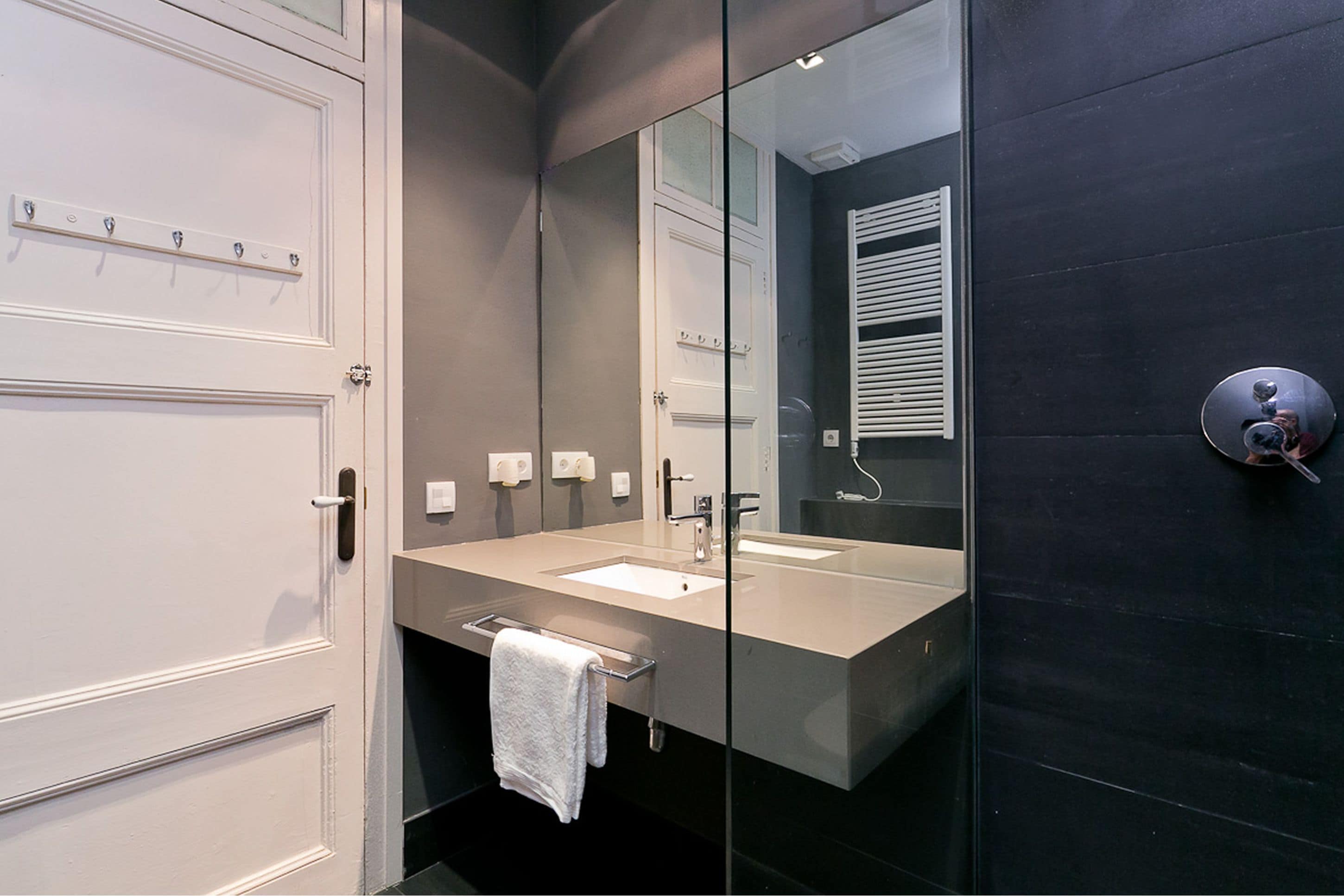 A modern bathroom with a glass shower enclosure, a large mirror, and a white towel hanging on a rack.