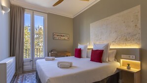 A hotel room with a large bed, a nightstand, a ceiling fan, and a view of the city through the window. - BCN Paseo de Gracia Rocamora Apartments (Barcelona)